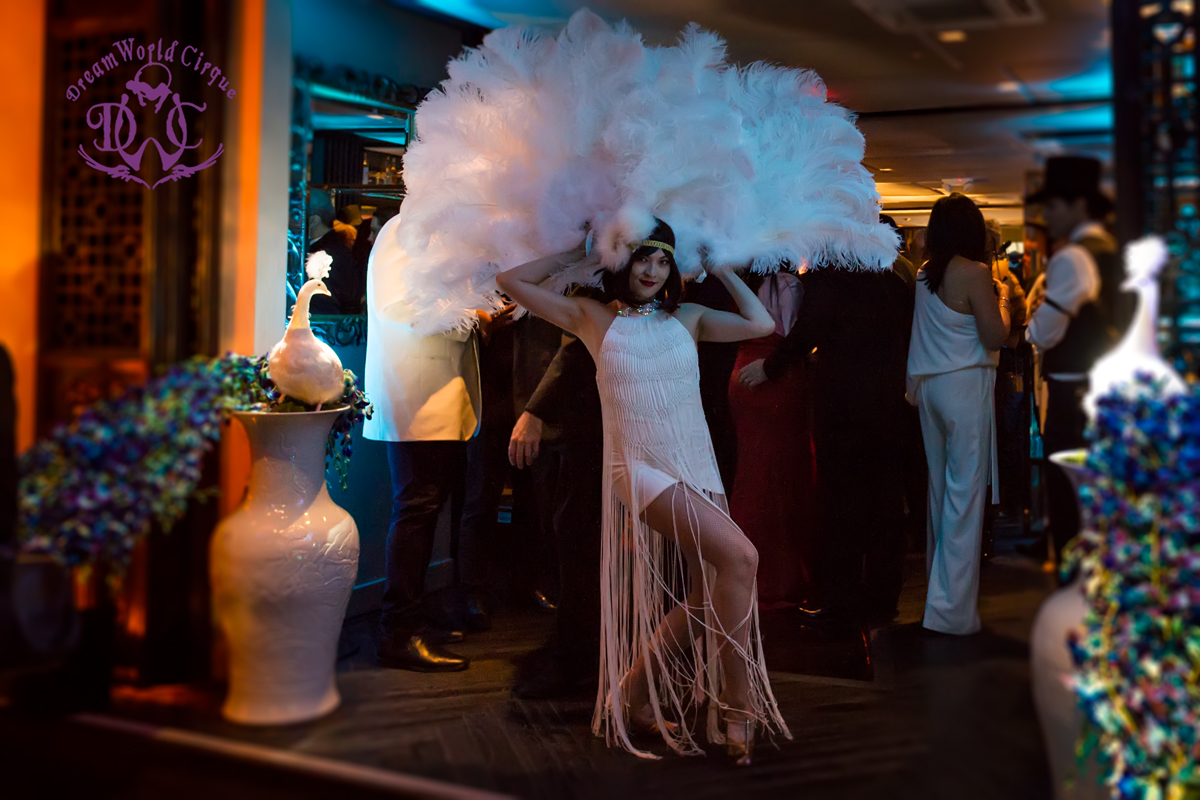 A beautiful dancer with large white feather fans captivates guests with her graceful poses and fluid movement
