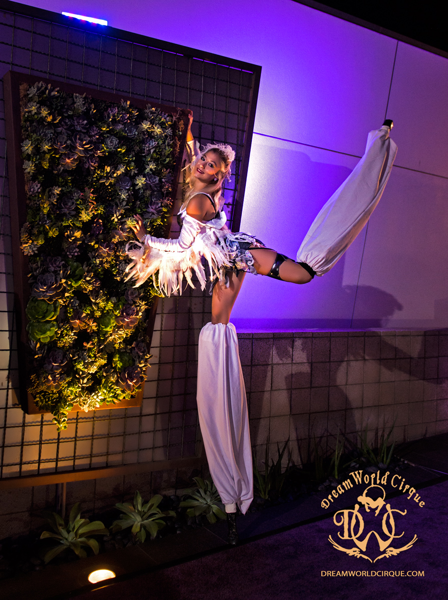 Ambient stilt performer with wings, shot from above in purple lighting