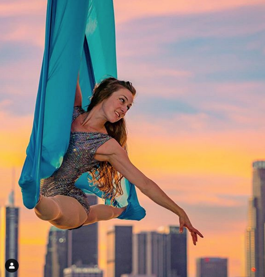 Aerial hammock performer against a sunset skyline